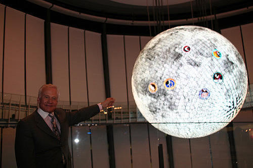 お台場・日本科学未来館の球体ディスプレイ「ジオコスモス」（宇宙から見た地球や月などを映し出す）を前にした、バズ・オルドリン氏。表示されているアポロ11号着陸地点を指す